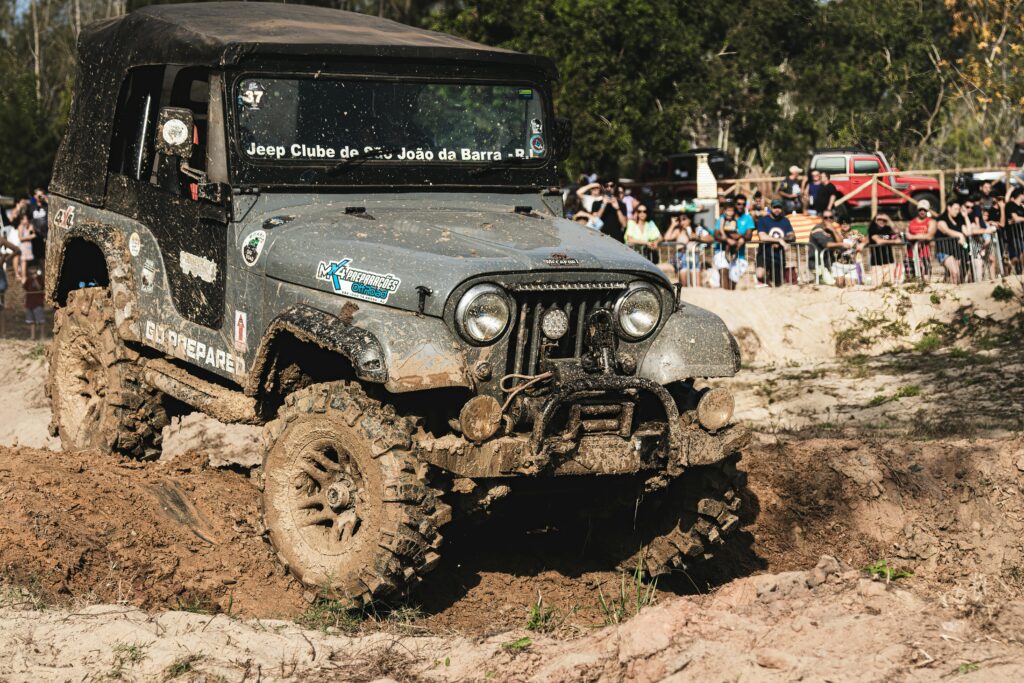 Jeep navigating a muddy track during an off-road event with spectators in the background.