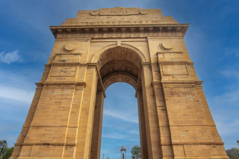 Stunning low-angle shot of the iconic India Gate monument in Delhi against a blue sky.