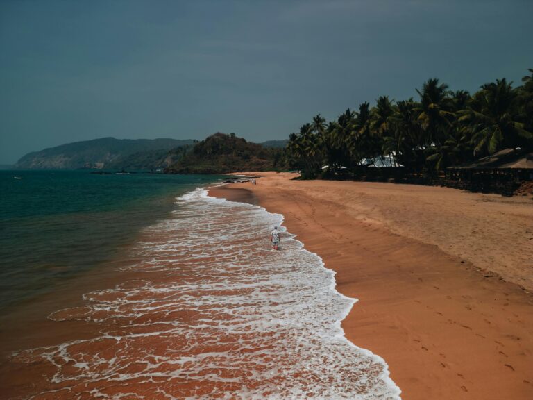 A picturesque aerial view of a serene beach in Goa with golden sands and gentle waves during sunset.