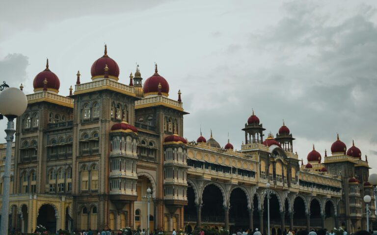 The grand Mysore Palace in India with its iconic red domes and intricate architecture under a cloudy sky.